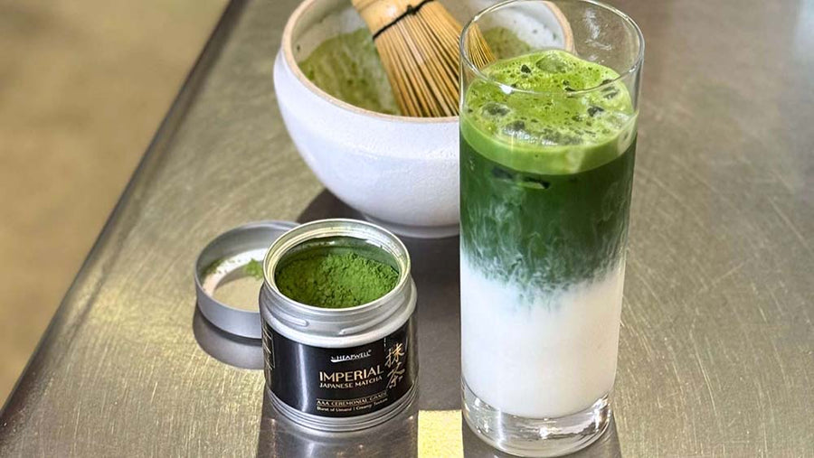 Matcha green tea powder, whisk, and glass of matcha latte on a metallic surface